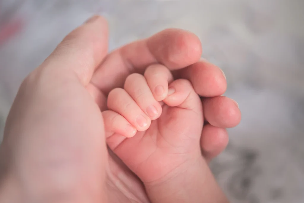Mão de bebê em close segurando a mão de um adulto